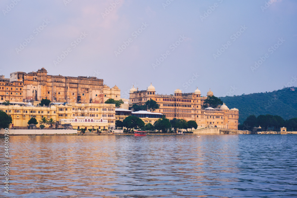 Obraz premium View of famous romantic luxury Rajasthan indian tourist landmark - Udaipur City Palace on sunset with tourist boat. Udaipur, Rajasthan, India