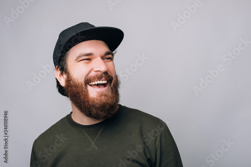 Close up photo of a cheerful bearded man wearing a cap with a large smile is looking aside. © Vulp