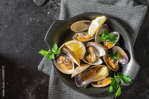 Cooked clams in a black ceramic plate on the black kitchen table. Seafood dish. The view from the top