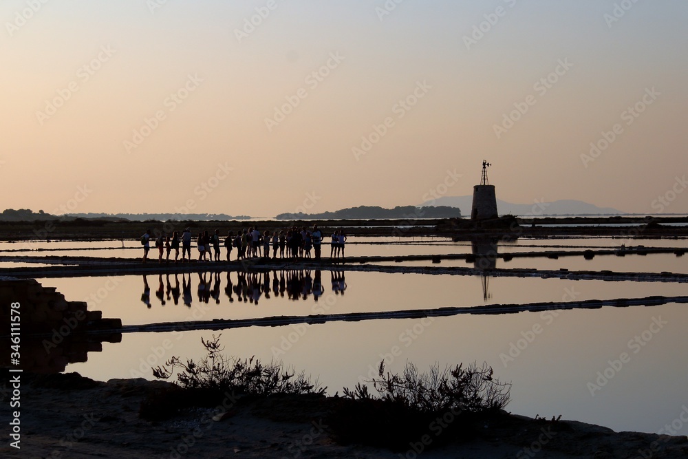 salt pans with water pumping tower and 
promontory in the background at sunset