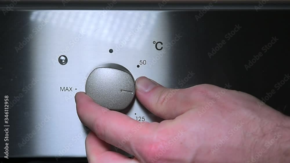 Adult person's hand operating the knob of the electric oven. Turning off the oven at home. Setting the temperature.