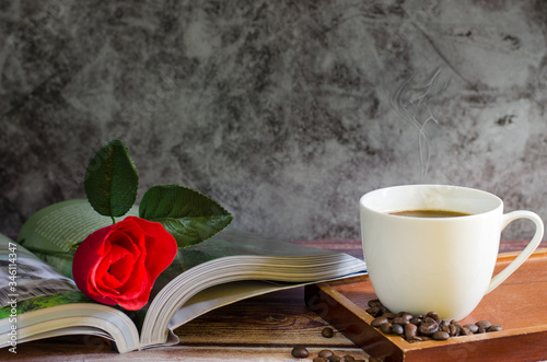 Hot coffee and coffee beans on an old wooden table and beautiful red roses in this book, cool summer drinks on dark wood floors with copy space.