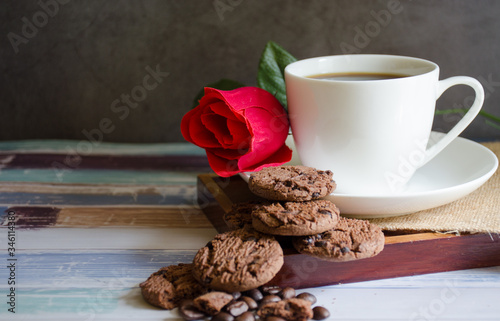 Coffee cups and chocolate chip baked cookies with red roses on a wooden table