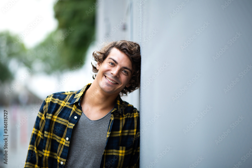cool young man leaning against wall outside and smiling cool young man leaning against wall outside and smiling