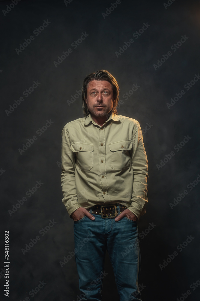Casual man in light brown shirt and jeans in front of grey wall. Low key studio shot.