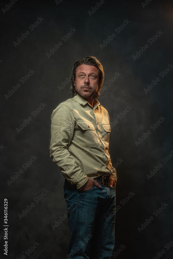 Casual man in light brown shirt and jeans in front of grey wall. Low key studio shot.