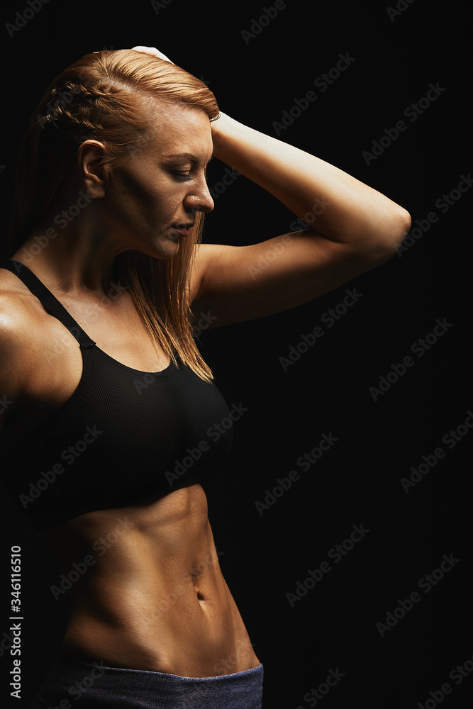 Naklejka premium Fitness fashion concept. Beautiful girl with a perfect sports figure posing on camera. ideal abdominal muscles, sports torso. On a dark background. Copy space