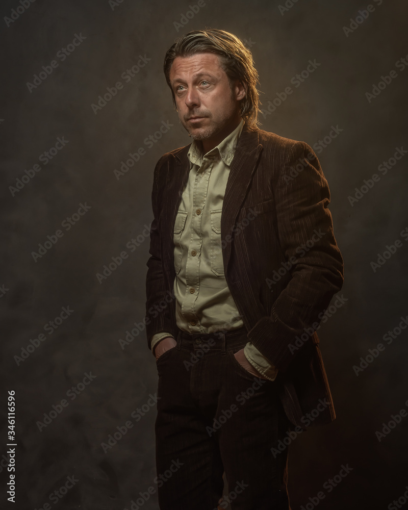 Fashionable middle aged man in dark brown suit in front of grey wall. Low key studio shot.