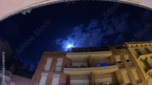 Night time lapse with moonlight and some stars on a cloudy sky in movement on a urban cityscape landscape photo