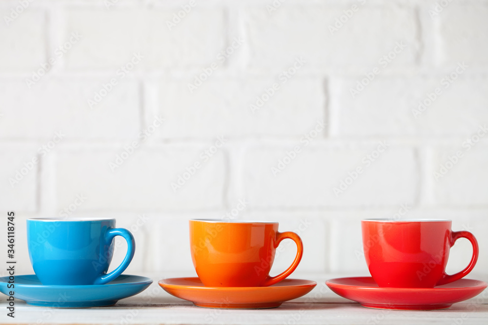 Obraz premium Colorful cups on the white background of a brick wall. Background with copy space. Horizontal. Selective focus.