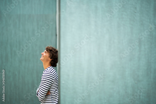  young smiling man leaning against green wall looking up