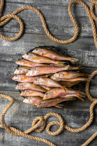 Black sea fish, red mullet in a black bowl on a gray wooden table. A lot of barabulka fish. Top view with space for text photo