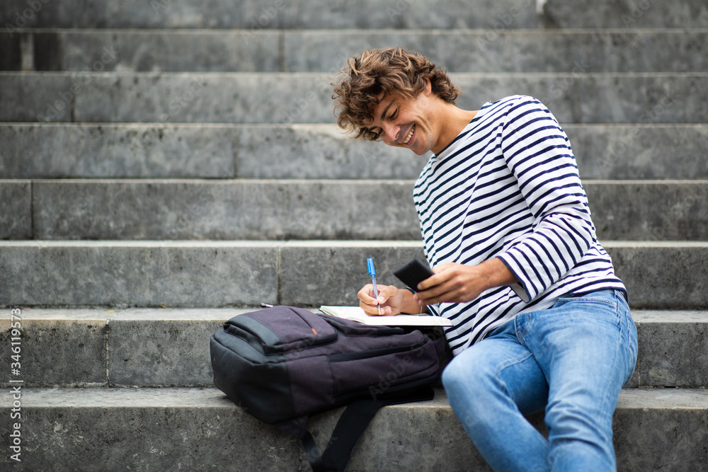 smiling male student sitting on steps outside writing in book
