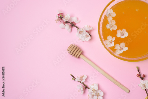 honey in a plate with a spoon and cherry flowers on a pink background. natural ingredient for skin care