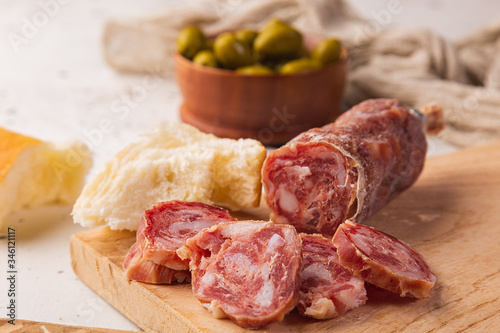 Sliced salami, bread, olives and cutting board on a white background, seen from the front