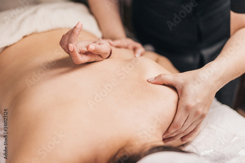 Hands of a masseuse on a female back during work - treatment of diseases of the back and spine - elimination of back muscle clamps