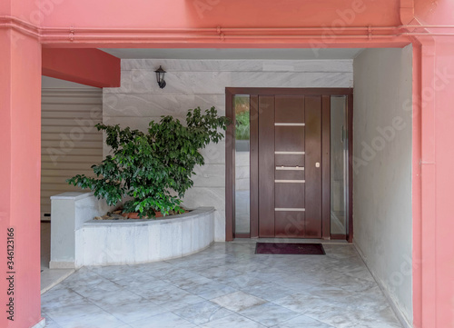 dark pink portico of apartment building entrance covered with white marble, potted plants and dark wood door
