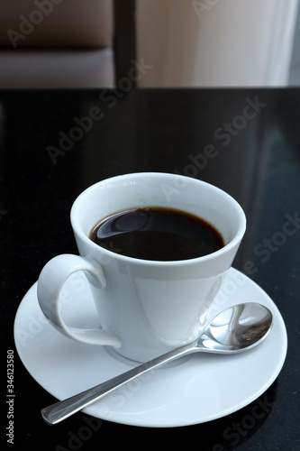 black coffee in a coffee cup  top view with saucers and spoon on a black table.