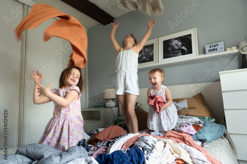 Three kids siblings rush and play in pile clothes