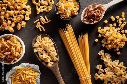 Heap of various raw pasta in different types and shapes on dark brown background photo