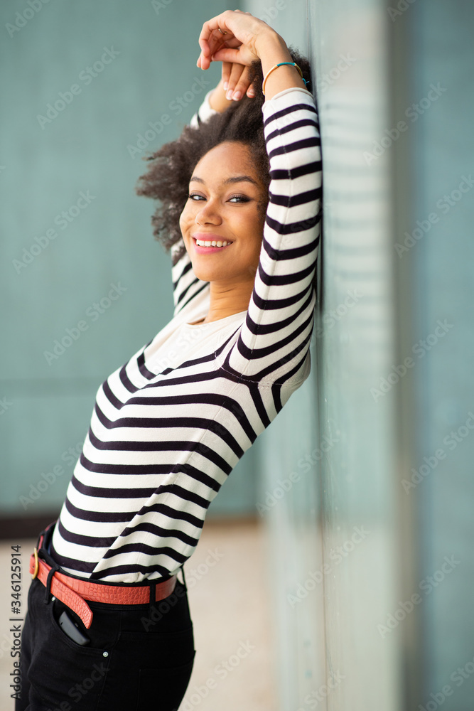Profile of smiling african american female fashion model leaning against wall