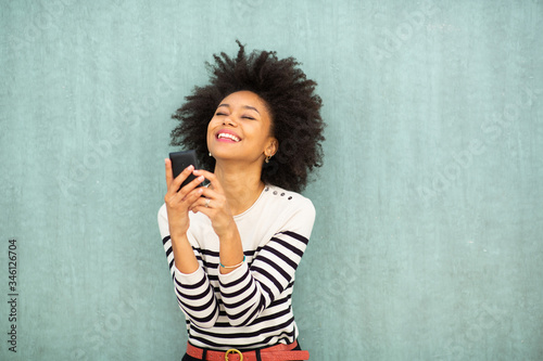 smiling young african american woman holding cellphone by green background