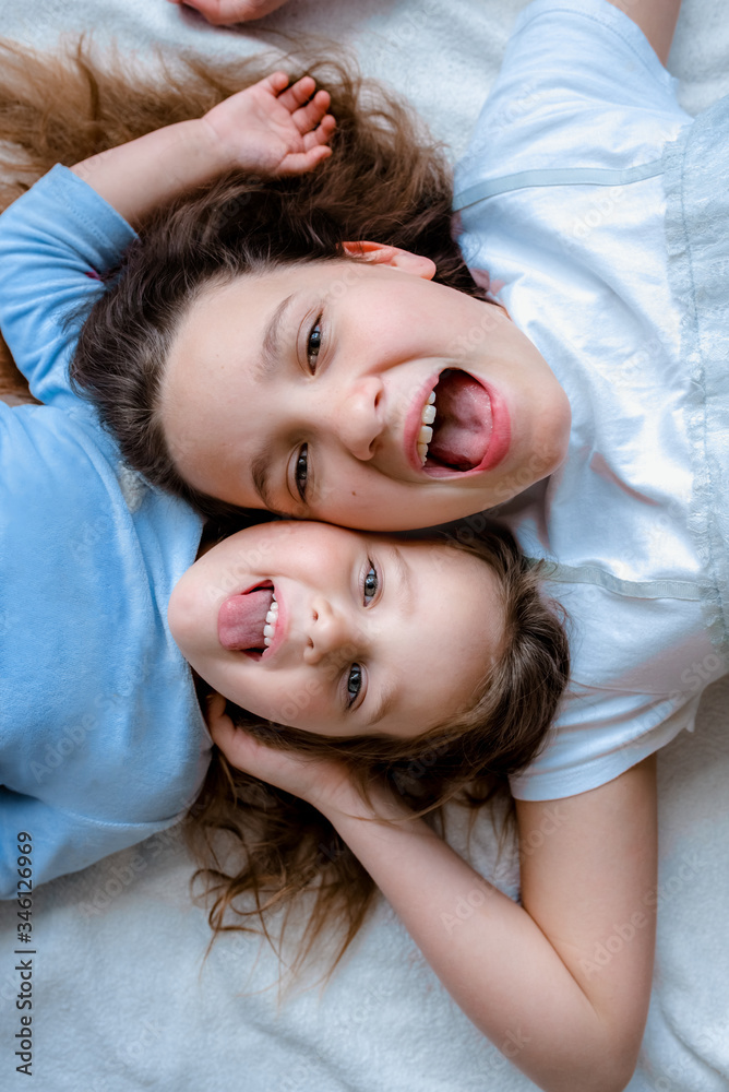 Portrait of two happy smiling kids having fun. Cheerful little girls lying laughing together on back top view sisters. Selective focus. Portrait of two happy smiling kids having fun. Cheerful little girls lying laughing together on back top view sisters. Selective focus.