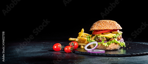Delicious burger with fried potatoes on a dark background