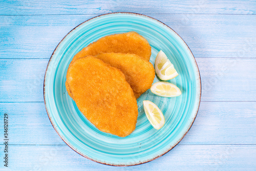 Top view, flat lay.Breaded chicken schnitzel on a blue plate with slices of lemon on a blue wooden background photo