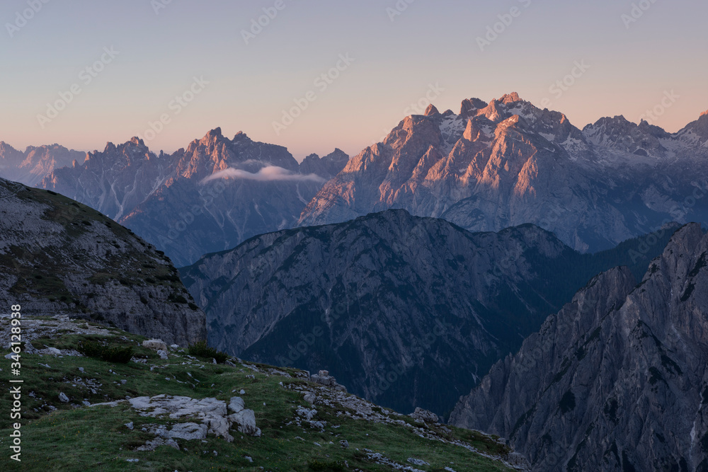 Mountain landscape in the European Dolomite Alps underneath the Three Peaks with alpenglow during sunrise, layers of mountains, South Tyrol Italy.