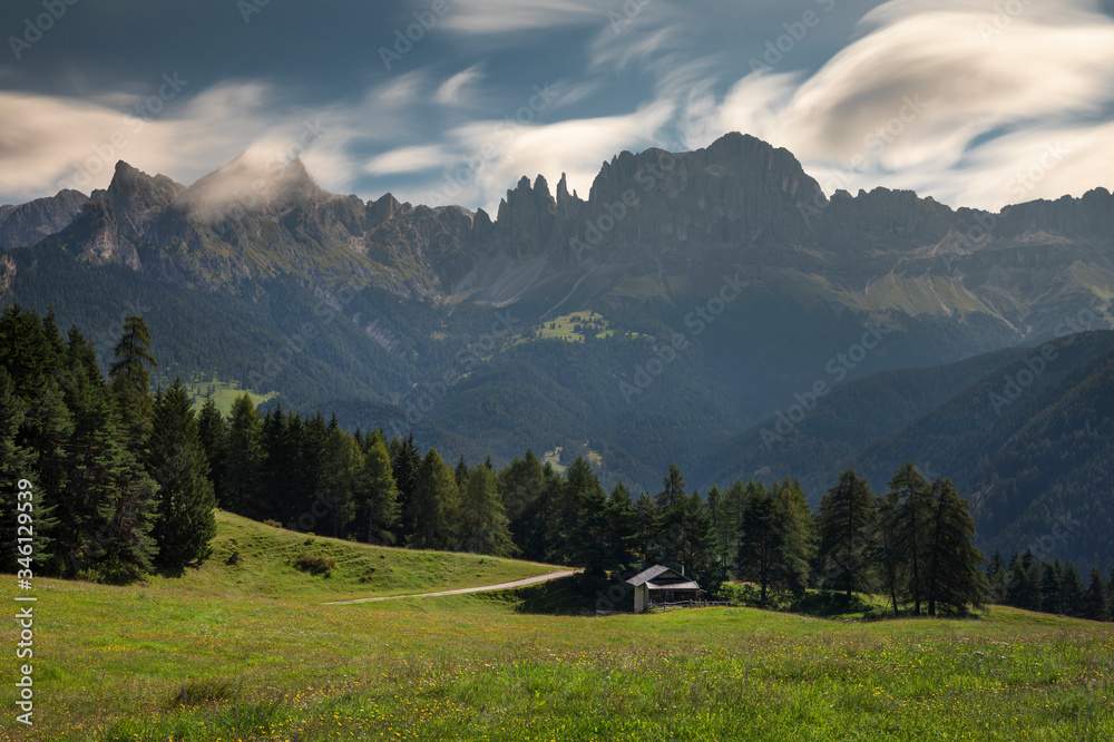 Rosengarten mountain range in the European Dolomite Alps with clouds in the sky, green meadow and trees, South Tyrol.