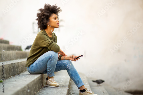 young woman sitting on steps with mobile phone and earphones