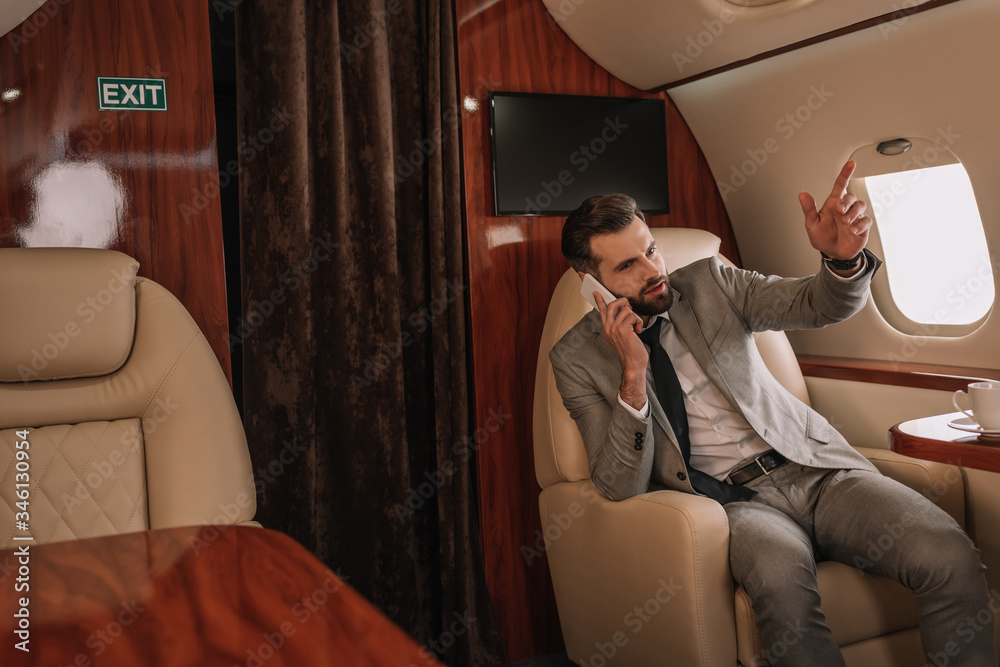 Obraz premium handsome businessman talking on smartphone and pointing with finger in private jet