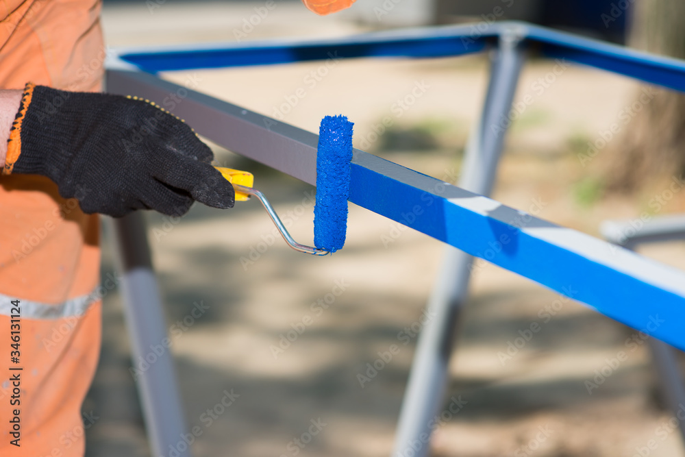 Worker in gloves with a roller paints metal blue Worker in gloves with a roller paints metal blue
