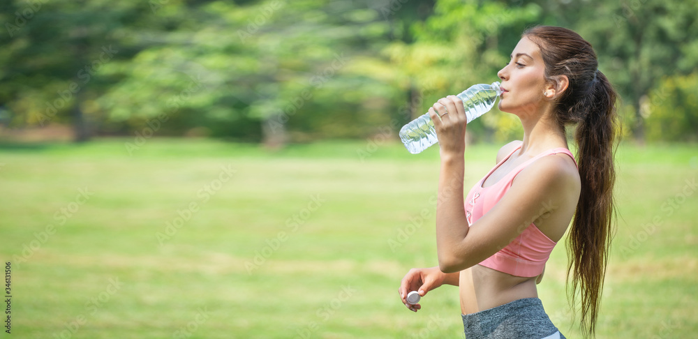 young fitness woman drinking water from plastic bottle after exercise at public park in morning . sport beautiful girl thirsty taking a break from workout in training . Panorama banner copy space . young fitness woman drinking water from plastic bottle after exercise at public park in morning . sport beautiful girl thirsty taking a break from workout in training . Panorama banner copy space .