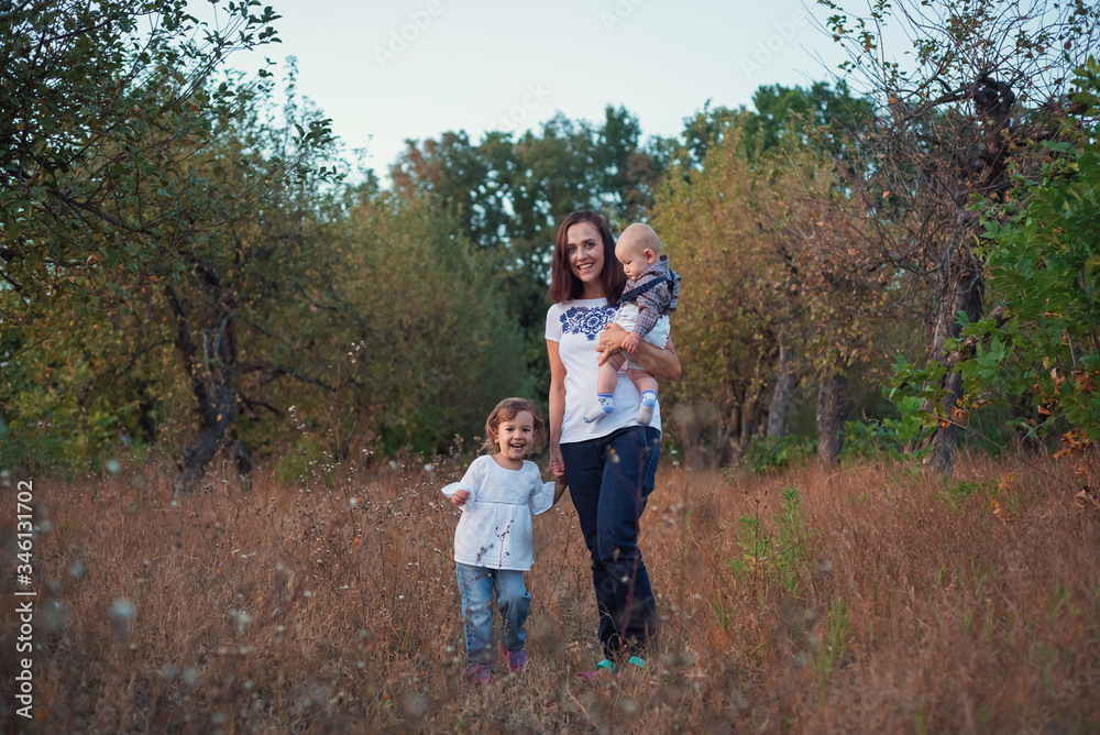 A stylish young mother with children in an apple garden autumn evening. A stylish young mother with children in an apple garden autumn evening.