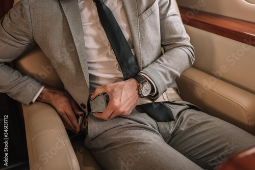 cropped view of businessman fastening safety belt while sitting in private jet