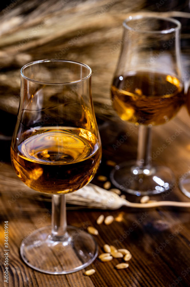 Tasting glasses with aged Scotch whisky or bourbon on old dark wooden vintage table with barley grains