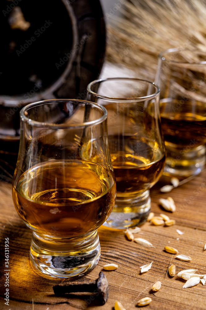 Small tasting glasses with aged Scotch whisky on old dark wooden vintage table with barley grains Small tasting glasses with aged Scotch whisky on old dark wooden vintage table with barley grains