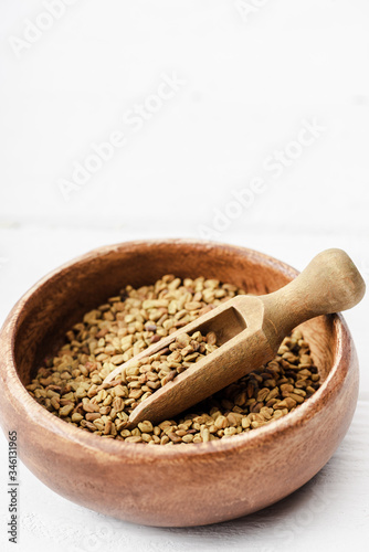 natural fenugreek in wooden bowl with spatula on white surface © LIGHTFIELD STUDIOS