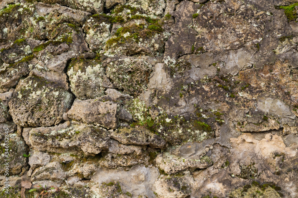 Stone texture at the foot of a mountain or cliff or cave wall, dotted with grooves and covered with moss