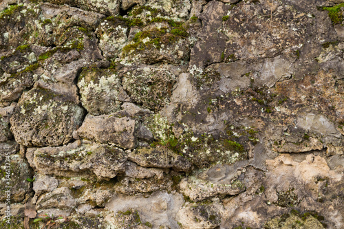 Stone texture at the foot of a mountain or cliff or cave wall, dotted with grooves and covered with moss