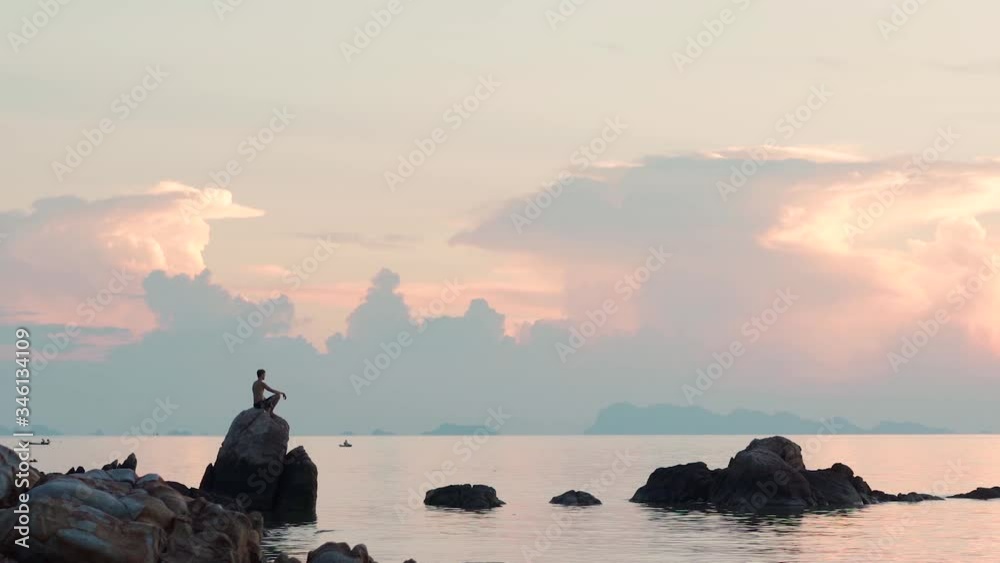 Man sitting on a rock in the lotus position and looking at the setting sun Man sitting on a rock in the lotus position and looking at the setting sun
