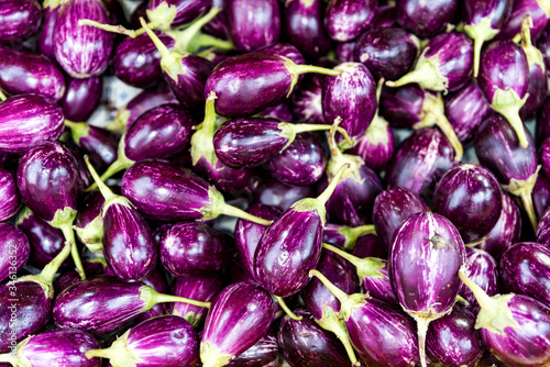 Fototapeta Naklejka Na Ścianę i Meble -  Close up of small purple Asian eggplants. Top view of fresh organic eggplants or brinjal at street market. Purple vegetable background 