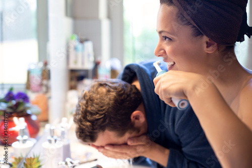 Coppia si prepara in bagno divertita: lui si lava la faccia e lei si lava i denti con lo spazzolino elettronico