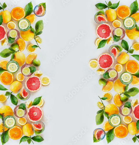 Frame of various colorful citrus fruits  lemon  lime  orange and grapefruit with green leaves and glasses of refreshing lemonade drinks on white background  top view. Healthy lifestyle. Layout.