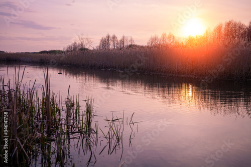 Magical sunset in countryside. Rural landscape in spring, wilderness. Narrow river in evening