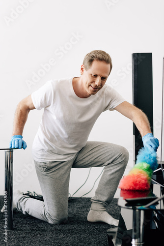 selective focus of cheerful man holding duster brush while cleaning apartment