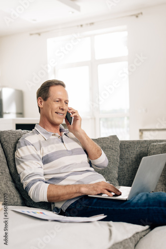 selective focus of cheerful freelancer talking on smartphone and using laptop at home