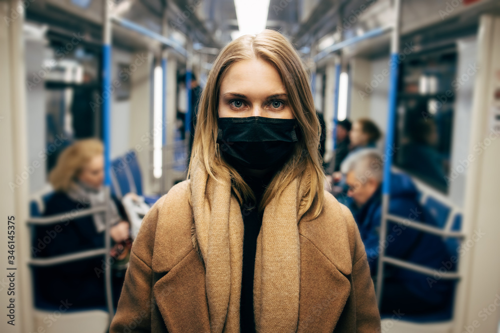 Blonde woman in black medical mask standing in subway car.